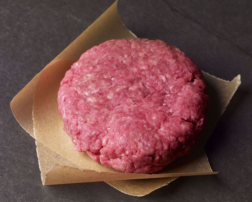 Slate table with  2 - brown parchment squares and a raw burger patty on top