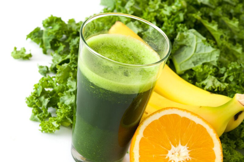 This photo shows a green drink, a bunch of kale, two bananas, and a halved orange against a white background, representing the 12 best foods for the nervous system.