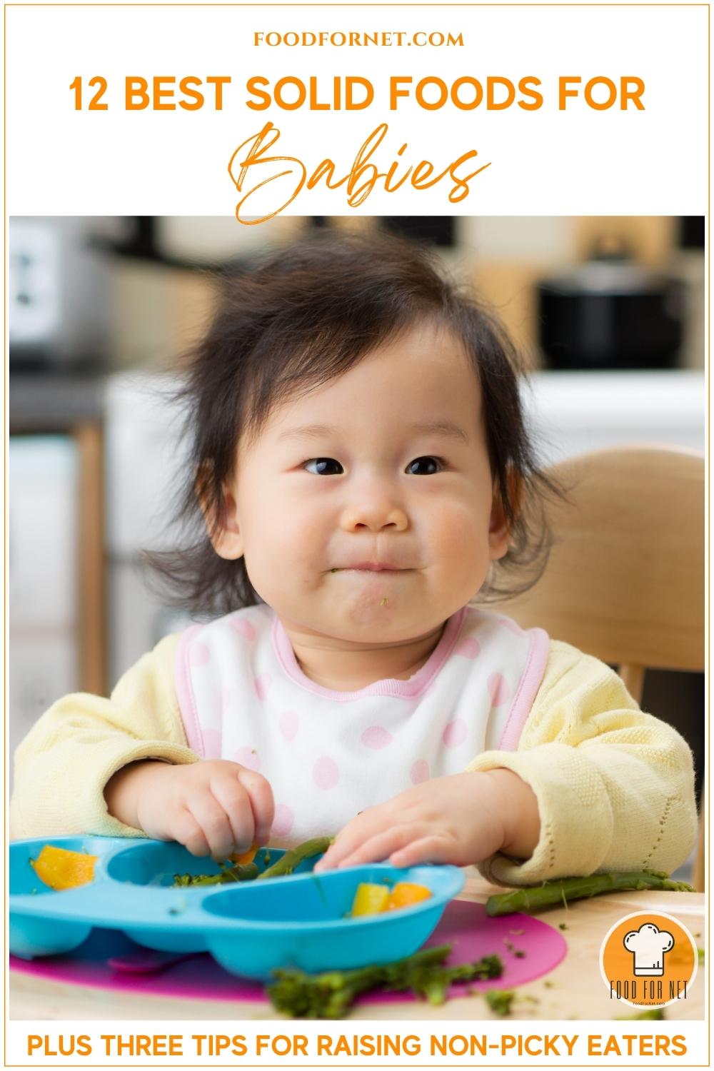 baby in yellow long-sleeved top and white and pink bib, eating broccoli and orange vegetables on her blue baby plate; with text overlay "12 Best Solid Foods For Babies, Plus Three Tips For Raising Non-Picky Eaters"