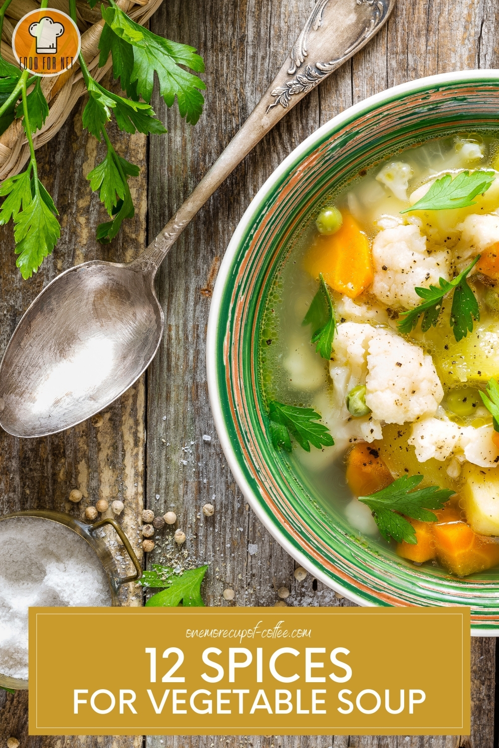 Top view of a bowl of vegetable soup laid out on a wooden table with silver spoon, salt, herbs, and spices around it.