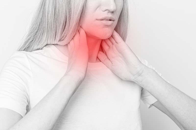 15 Best Foods Hyperthyroidism | Food For Net In this mostly gray and white photo,, a blonde woman in a white tee shirt holds her hands up to her neck, which is red.