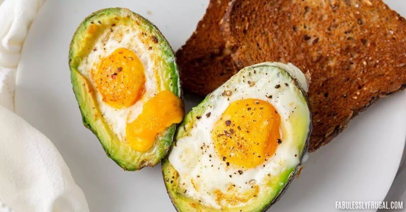 Two avocado and eggs that were baked in an air fryer, next to a piece of toast