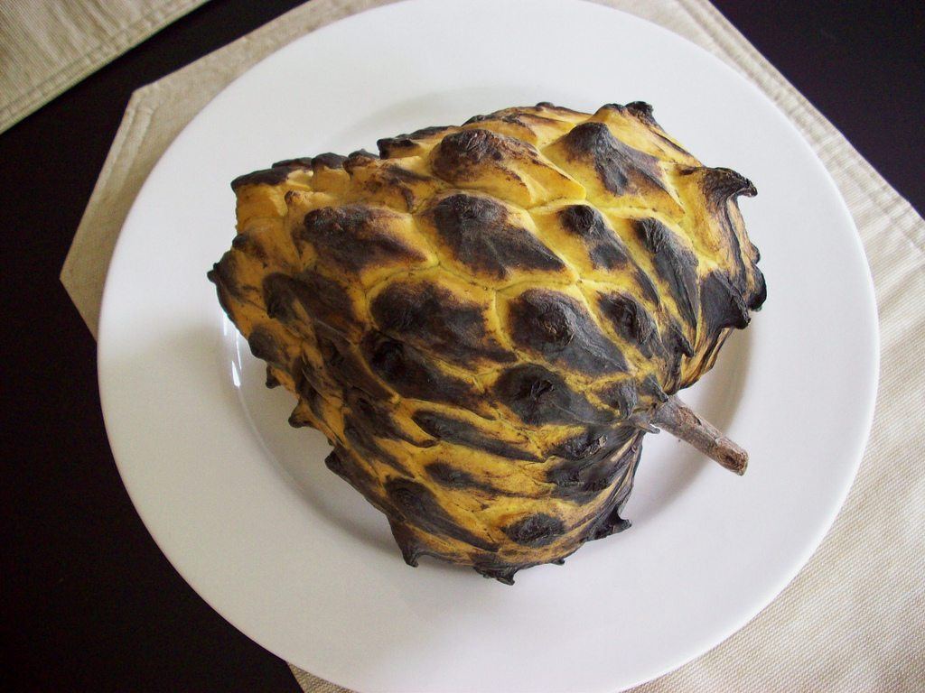 A white plate with a black and yellow fruit called rollinia deliciosa or birbia