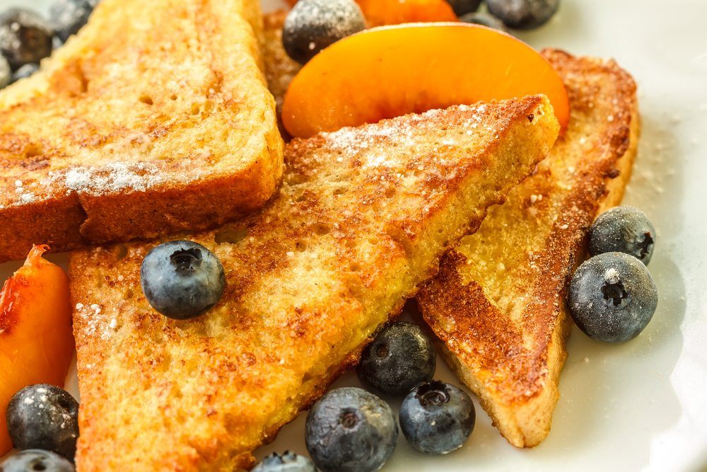 A white plate with pieces of French toast, peaches, and blueberries