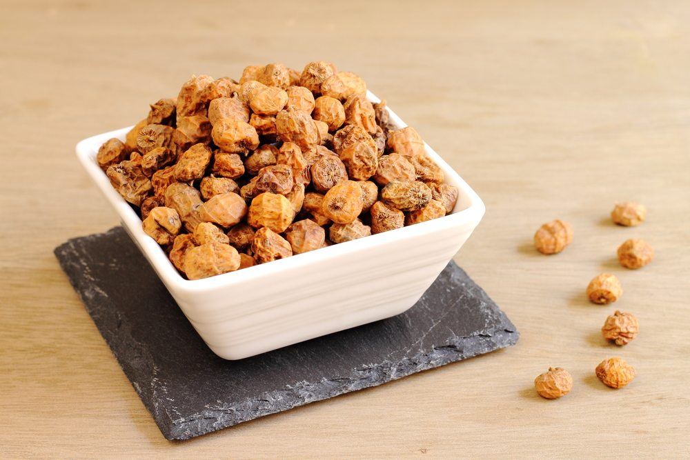 A decent white bowl containing tiger nuts on a black slate, with a few tiger nuts scattered on the table. 