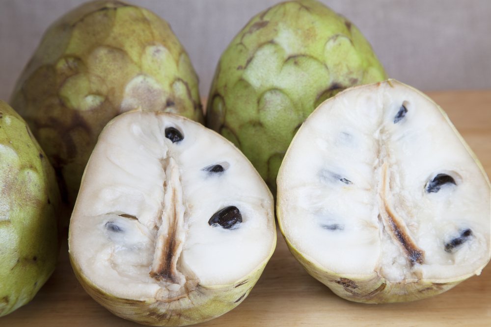 Whole cherimoya fruits on a table, along with two halves