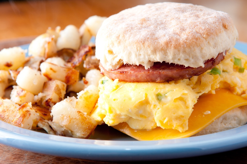 A light blue plate with a sausage, egg, and cheese roll and potatoes 