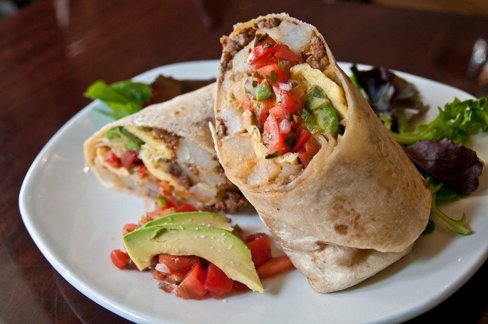 A white plate with two breakfast burritos, lettuce, salsa, and avocados