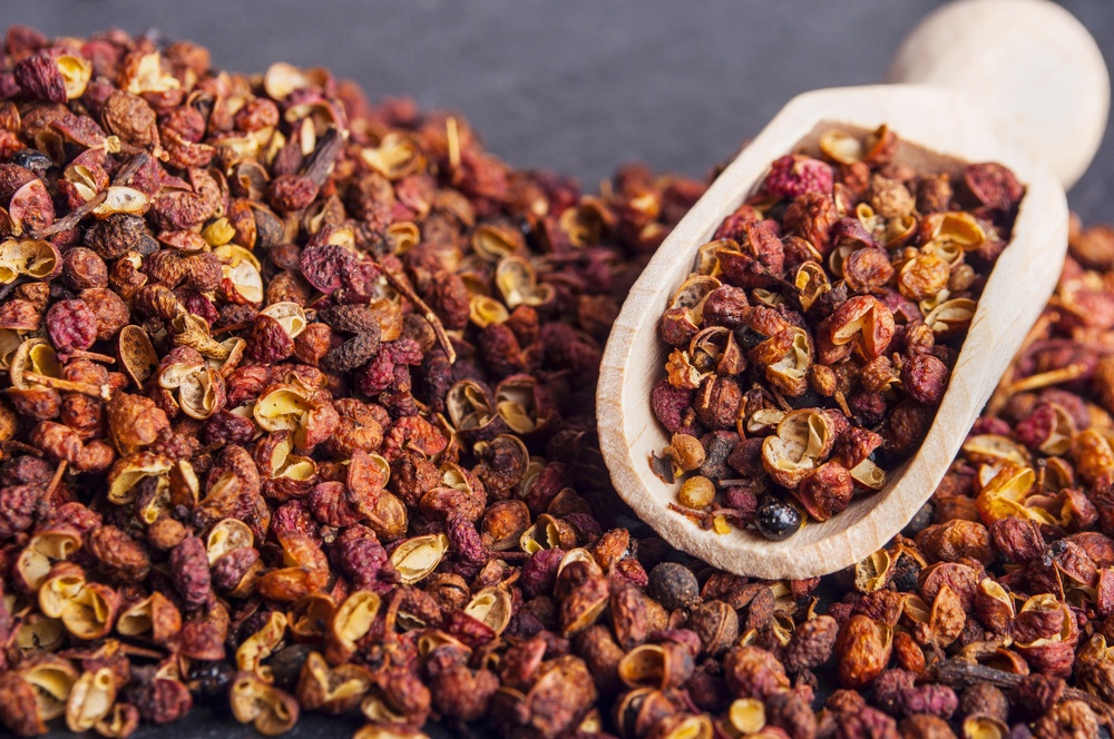 A large pile of szechuan peppercorns, with a wooden scoop