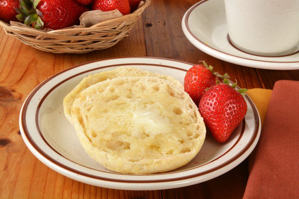 A white plate with brown stripes, two English muffin halves and strawberries