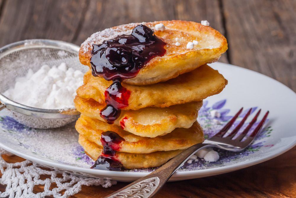 A blue and white plate with a stack of griddlecakes and jam, next to some icing sugar