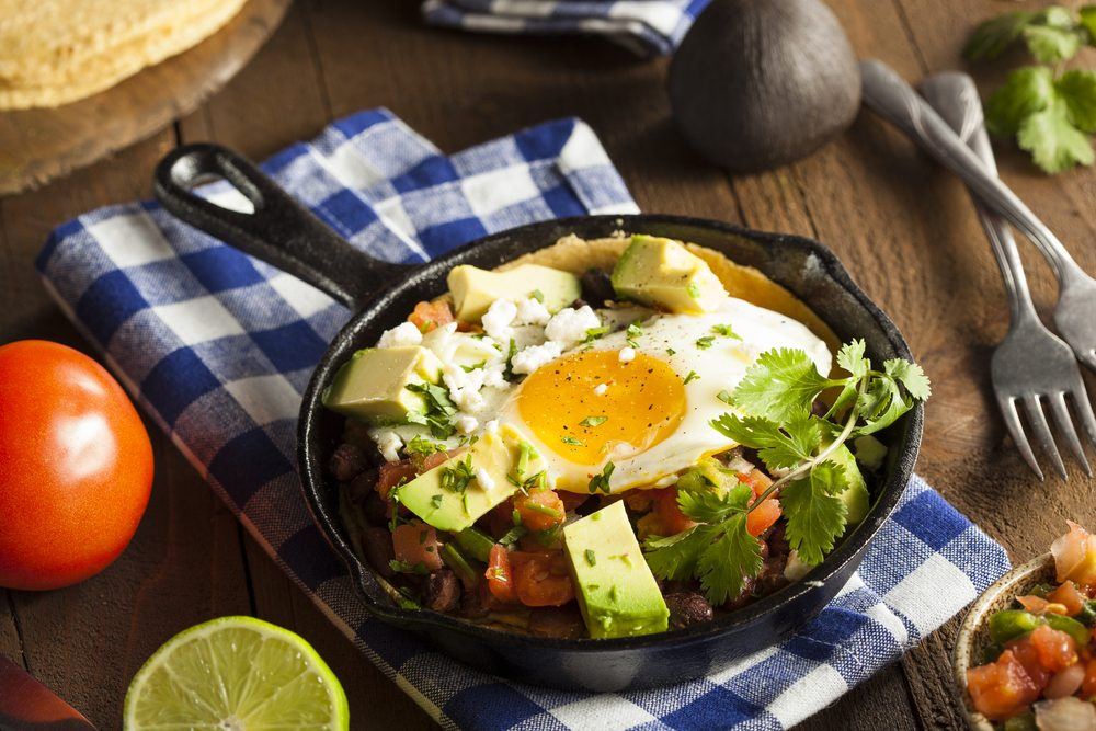 A small cast iron pan with huevos rancheros on a blue and white cloth