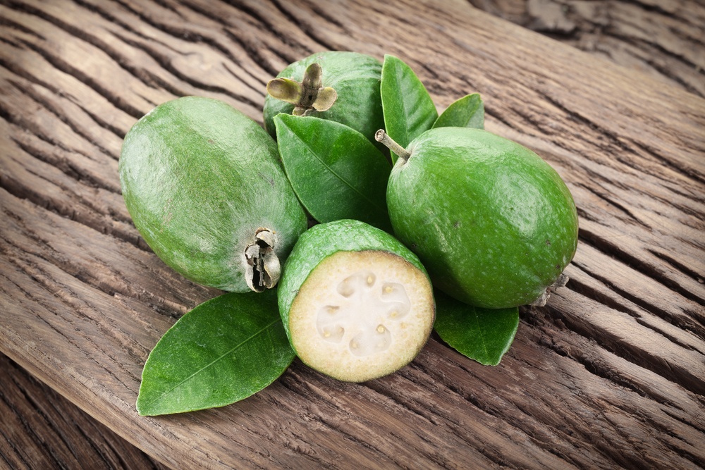 A collection of feijoas on a wooden board. Three are whole and one has been cut in half. 