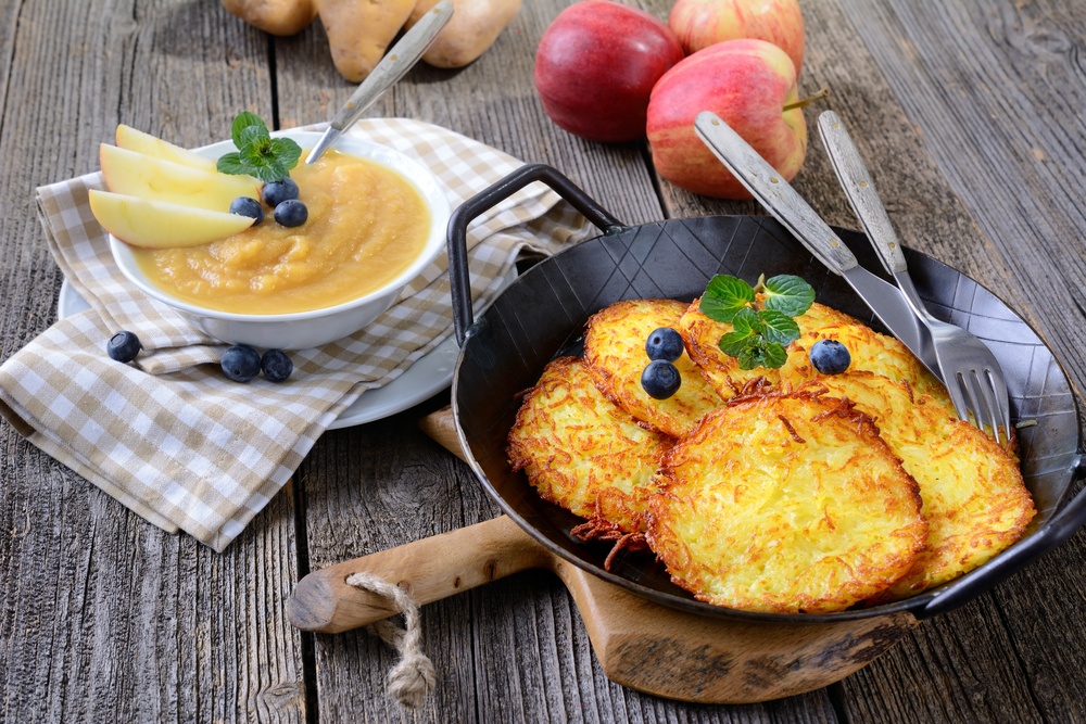 A black dish filled with potato pancakes, next to a dish of applesauce