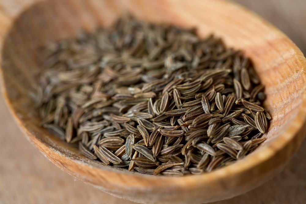 A wooden bowl or spoon containing kala jeera seeds