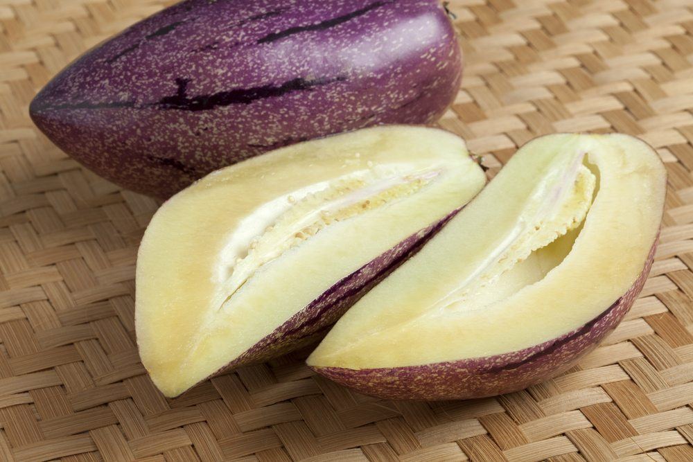 A purple fruit called the pepino melon. There is one whole version of the fruit and one that has been cut in half. 