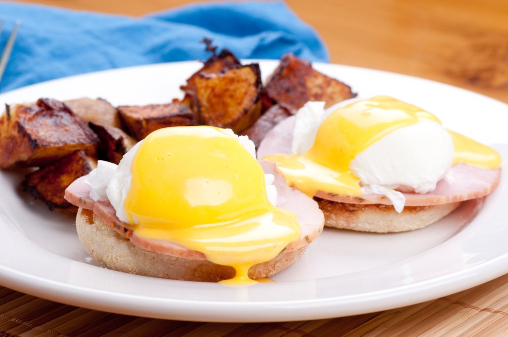 A large white plate with two English muffin egg benedicts, plus fried potatoes