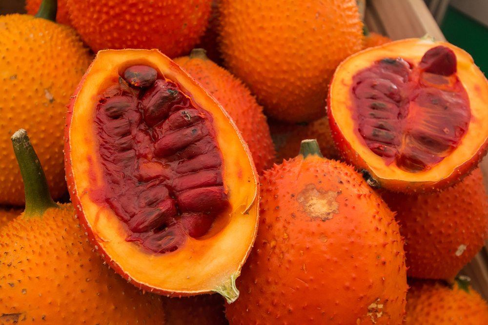 A bright orange fruit called gac, which is sometimes known as baby jackfruit. A variety of them are in a pile, including one that has been cut in half