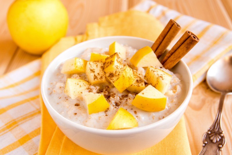 A white bowl filled with porridge, with chopped fruit and cinnamon 