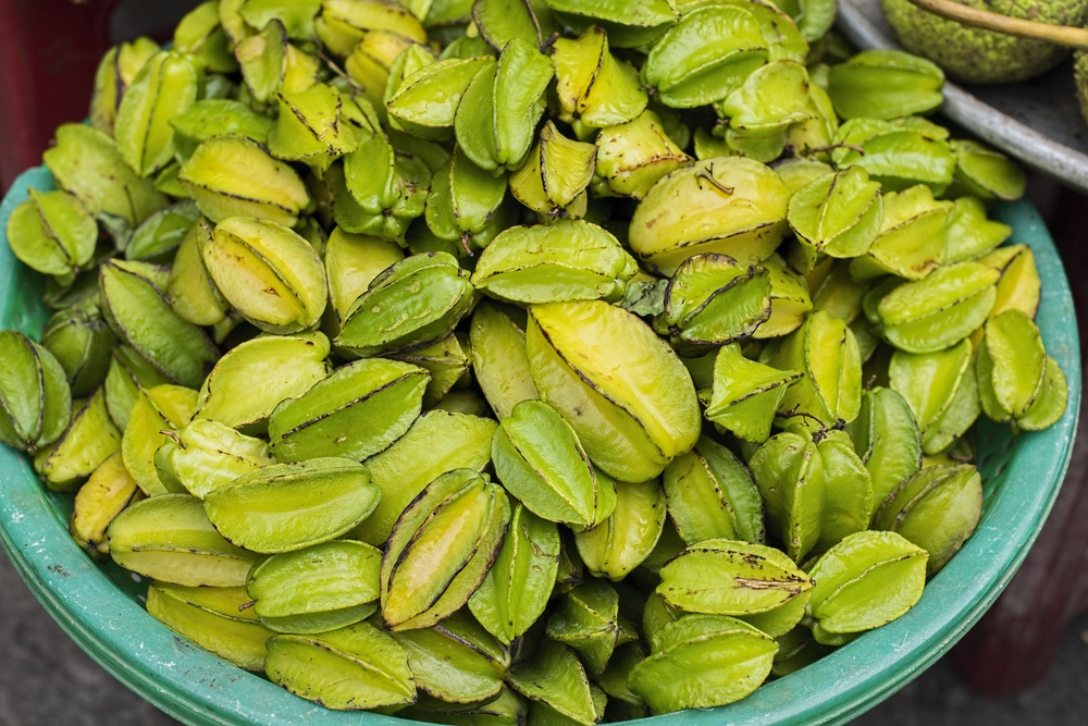 A large teal bowl containing many green starfruit of various sizes