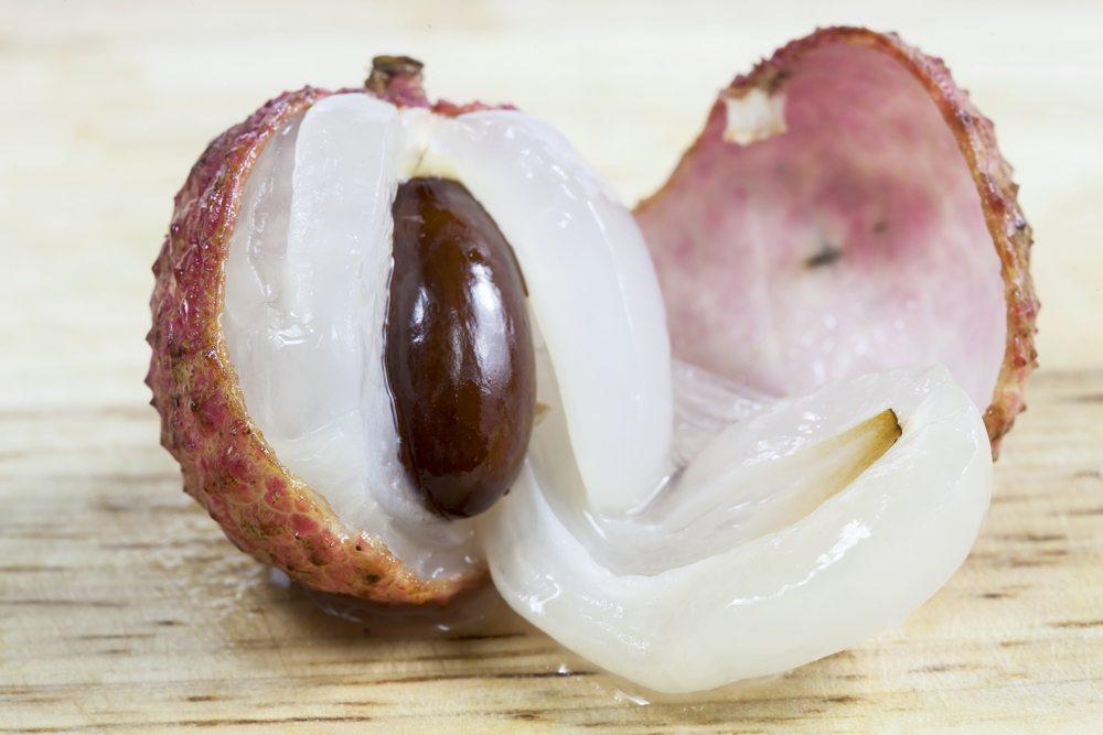 A purple lychee that has been partially peeled to reveal white flesh and a large pit