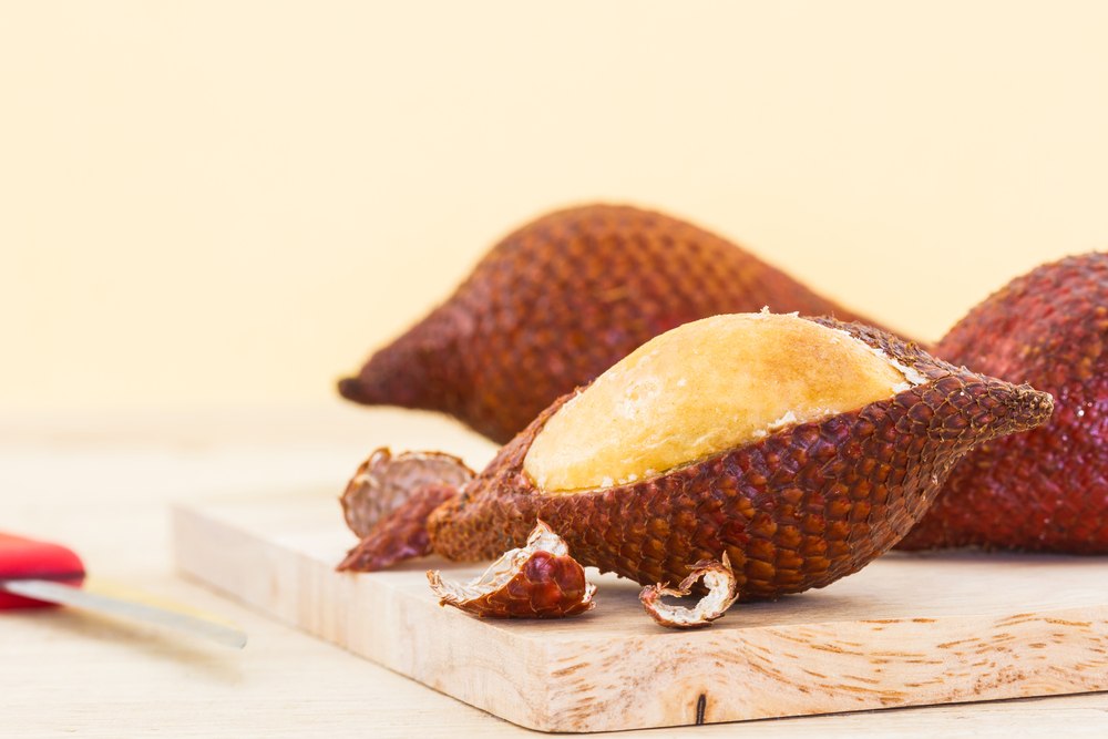 A wooden board with a few pieces of snake fruit or salak, one of which has been peeled to reveal light colored flesh