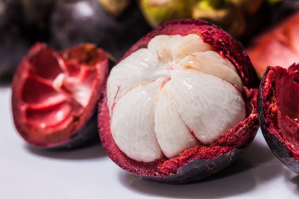 A purple mangosteen that has been partly peeled, showing its white flesh