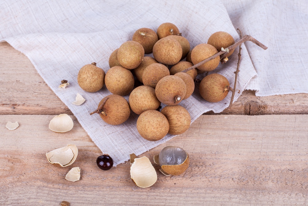 A collection of longan fruits. Most are still sealed, but one has been opened so that the flesh and seed can be seen