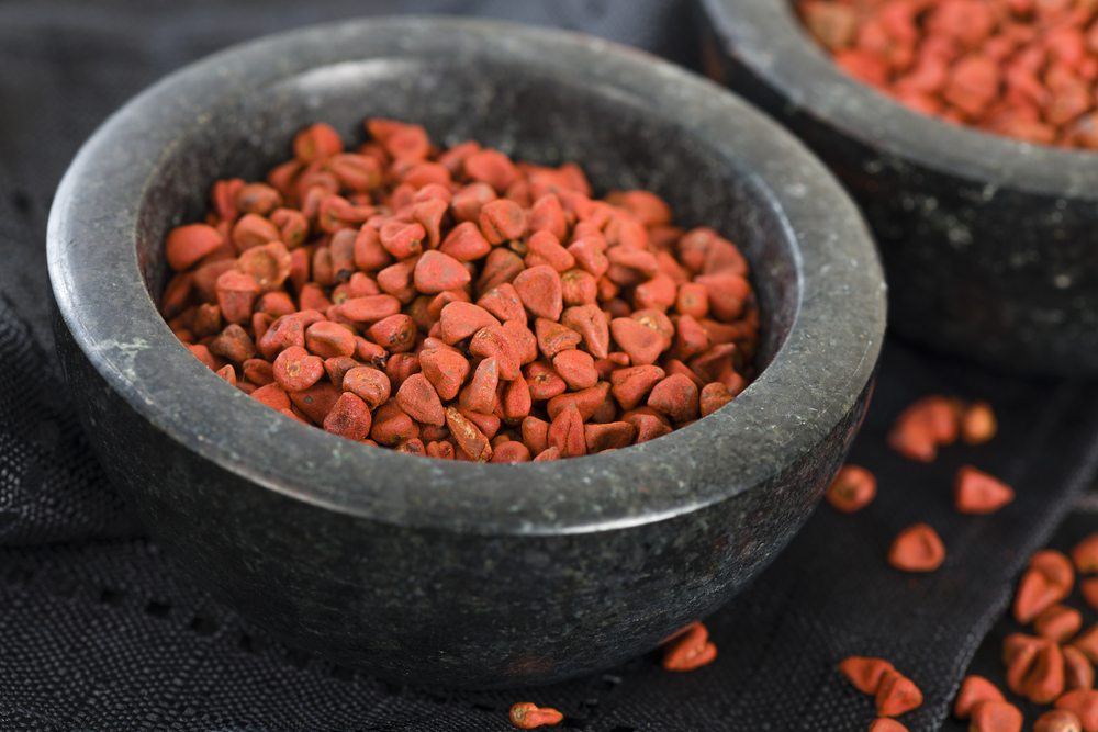 Two large black bowls containing many annatto seeds, with some more scattered outside the bowls