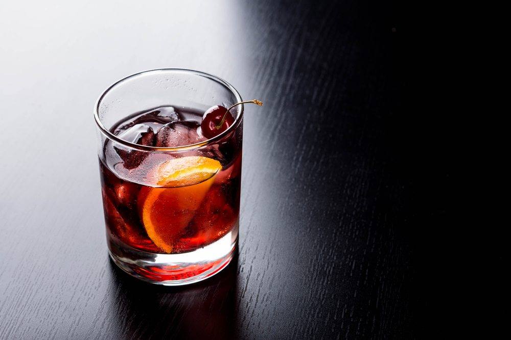 An old fashioned cocktail on a black bar with ice and a lemon slice