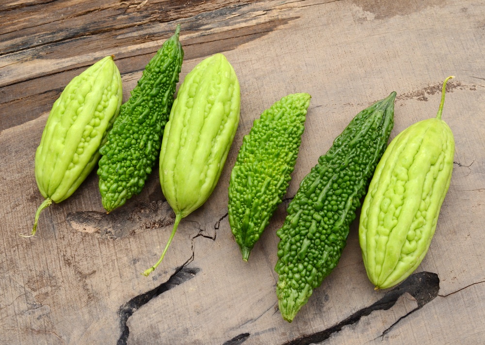 Six bitter melons lined up on wood, with different colorings and texture