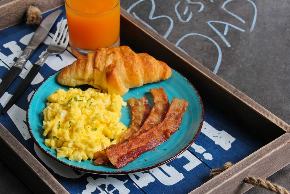 A tray with a blue plate with a croissant, bacon, and scrambled eggs