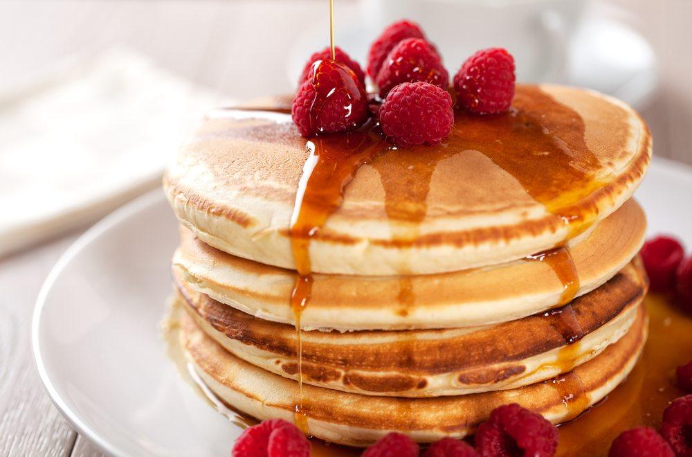 A light colored plate with a stack of pancakes, raspberries, and syrup