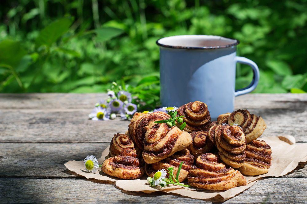 A wooden table with paper and a large pile of cinnamon rolls, plus a blue mug