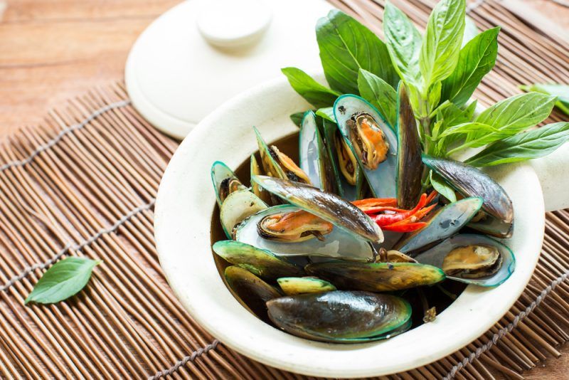 muscles cooked in stew with basil garnish on bamboo mat