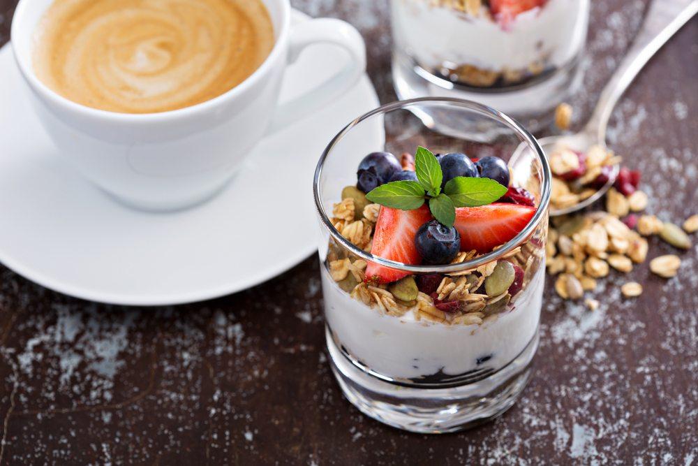 A glass containing granola, yogurt, and berries, plus a white mug of coffee