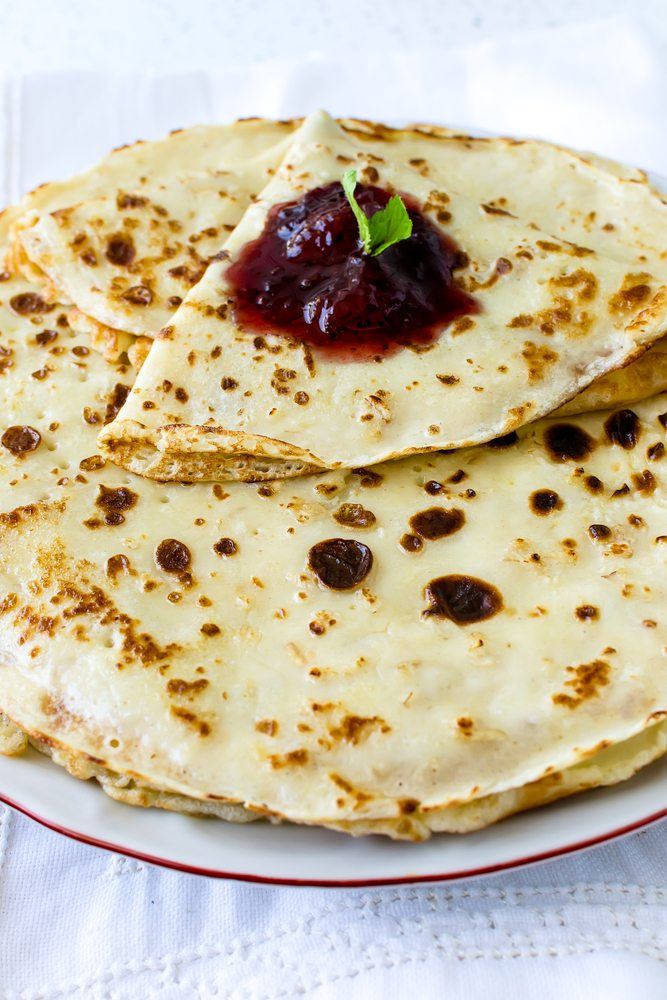 A white plate filled with thin crepes and jam