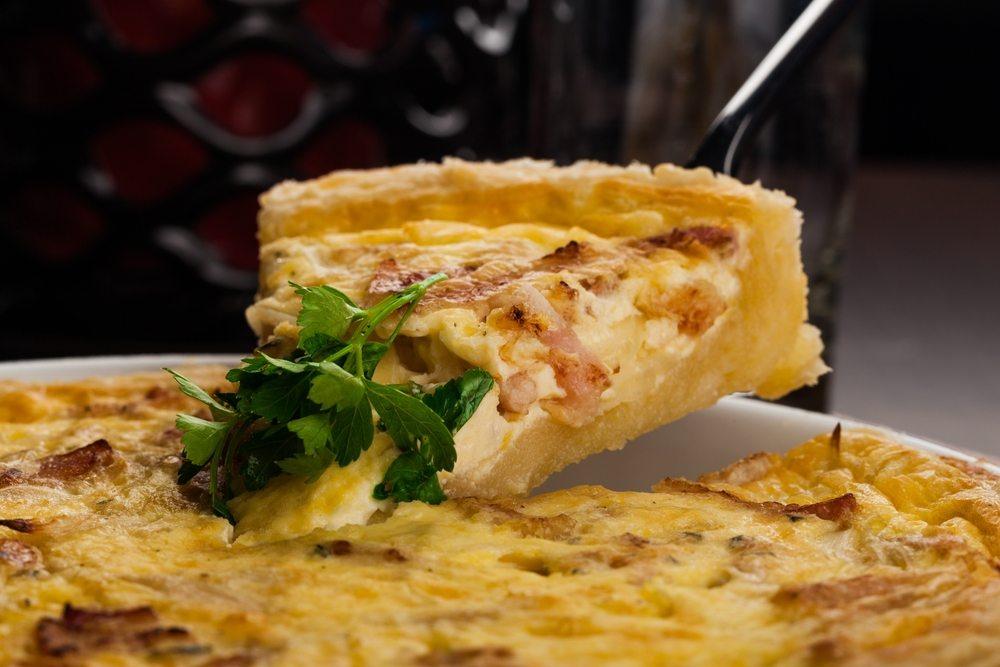 A whole quiche with a piece being removed