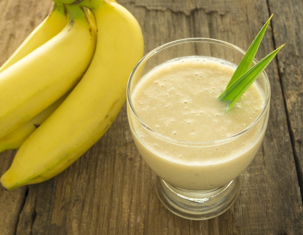 A glass filled with a banana smoothie next to fresh bananas 