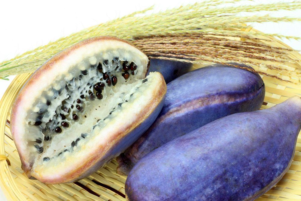 A purple fruit called akebi on a woven tray. Three pieces of the fruit are whole, while the last has been cut open. 