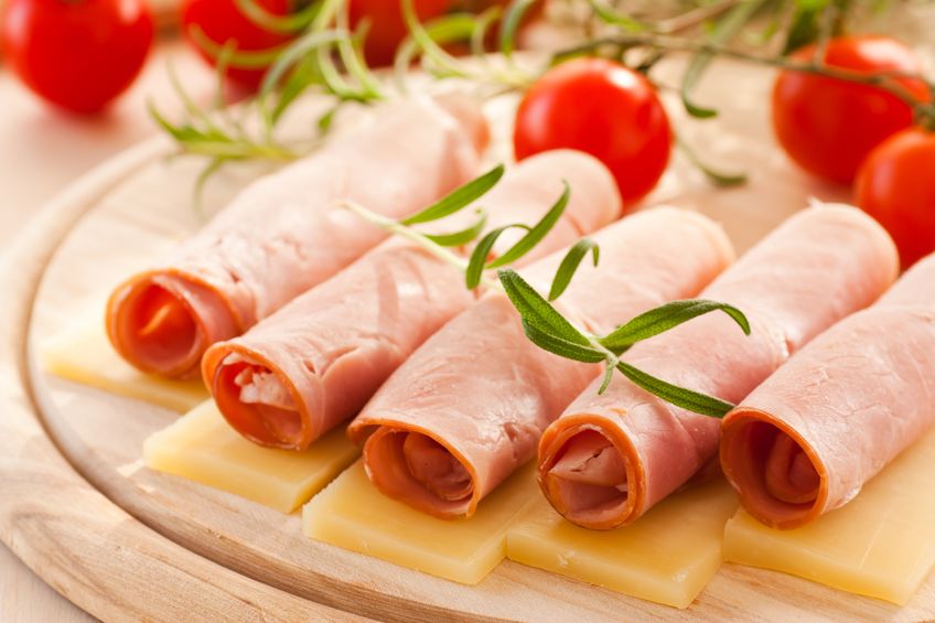 A wooden tray with cheese and rolls of ham, with cherry tomatoes 