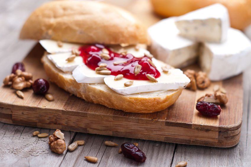 A wooden plate with bread, cheese, and jam