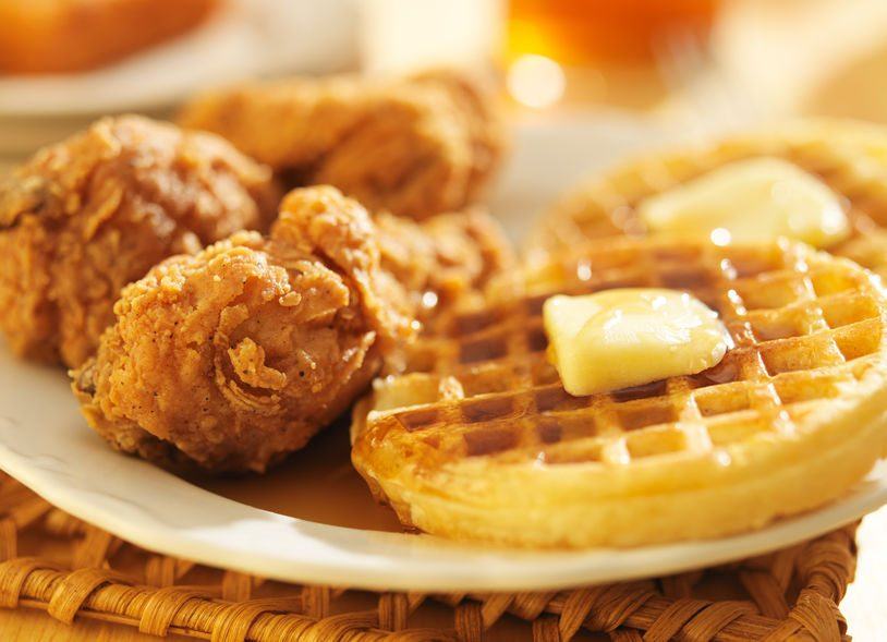 A white plate with waffles, butter, syrup, and fried chicken