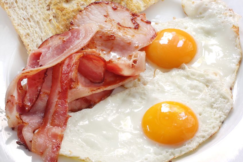 A white plate with a couple of sunny side up eggs, plus plenty of bacon and some bread 