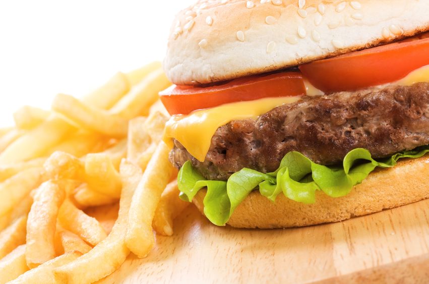 A wooden board with a whole burger and some fries