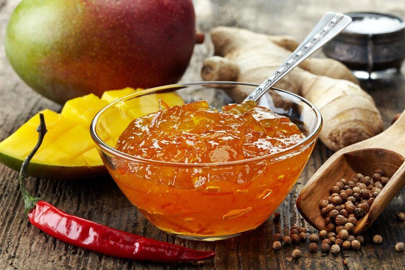 A glass bowl filled with mango chili chutney, with the ingredients scattered around