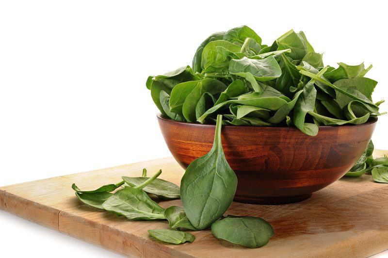 A wooden bowl of spinach on a wooden chopping board