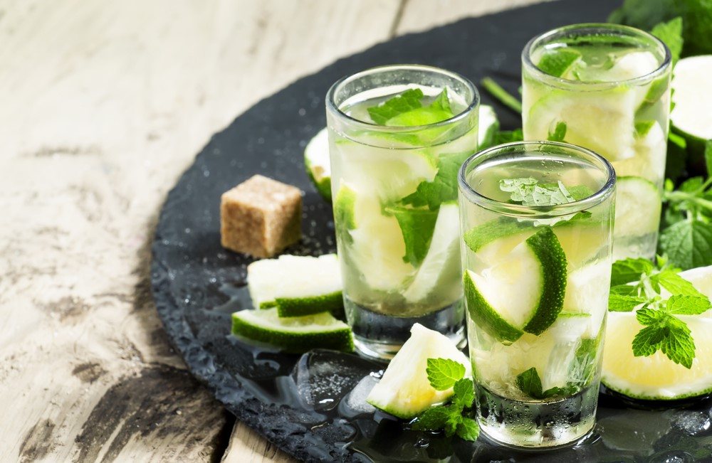 A large piece of slate with three Caipirinha cocktails and some of the ingredients scattered around