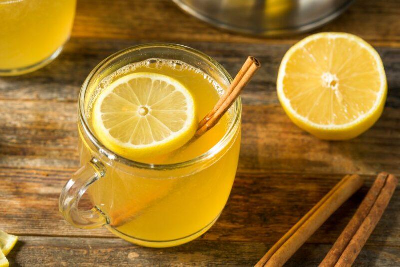 A wooden table with a Fireball hot toddy on it, half a lemon, and some cinnamon sticks