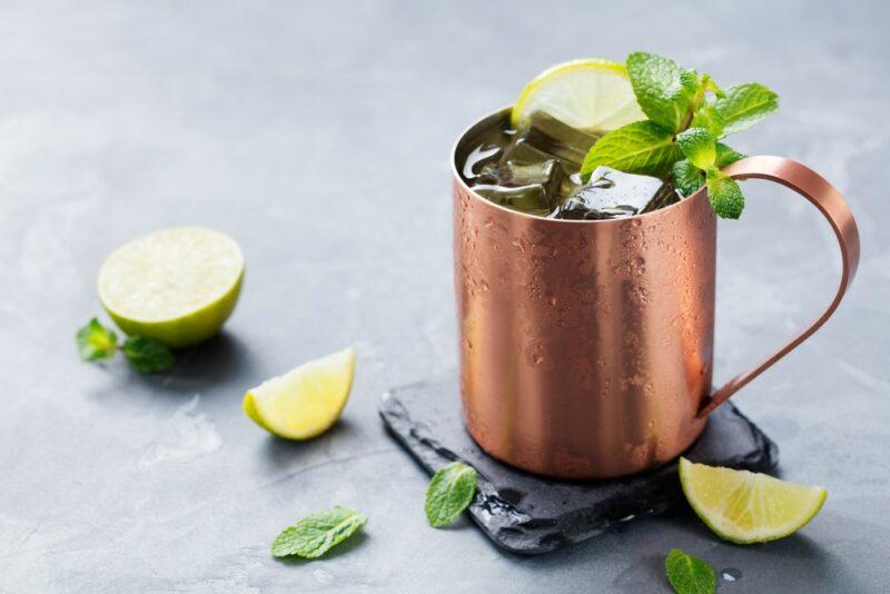 A Fireball mule cocktail in a copper mug on a table with lime wedges and peppermint leaves